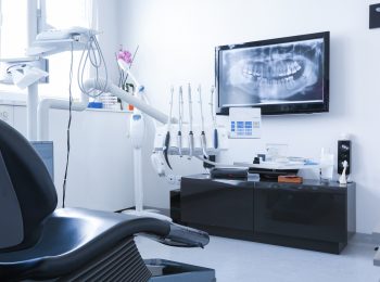Dentists chair and tools with x-ray picture on TV in the background. Dental care, dental hygiene, checkup and therapy concept.